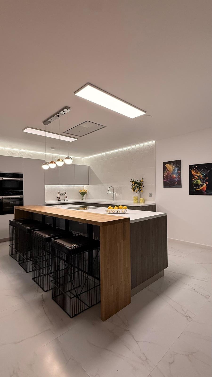 Cocina con isla de madera, encimera blanca, taburetes negros e iluminación LED Cocina con isla de madera, encimera blanca, taburetes negros e iluminación LED