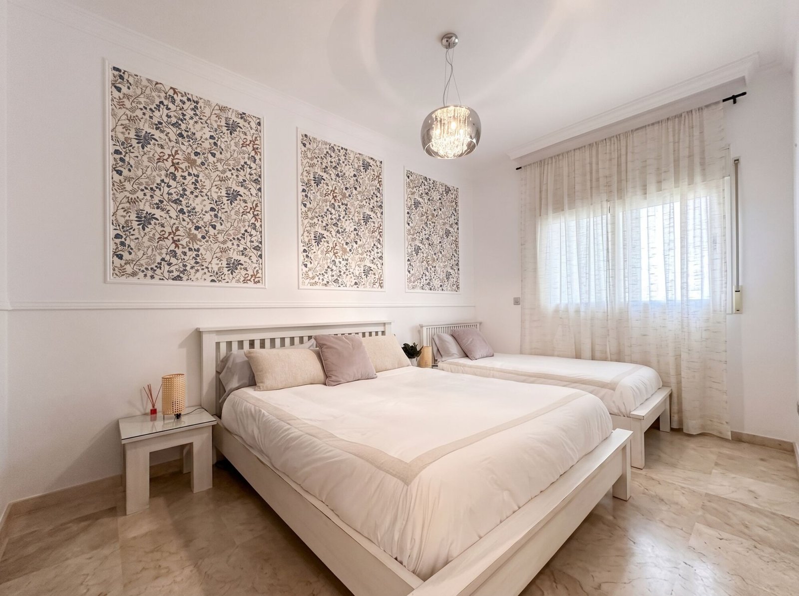 Apartamento San Roque: dormitorio con paneles de papel floral enmarcados, camas blancas y lámpara de cristal